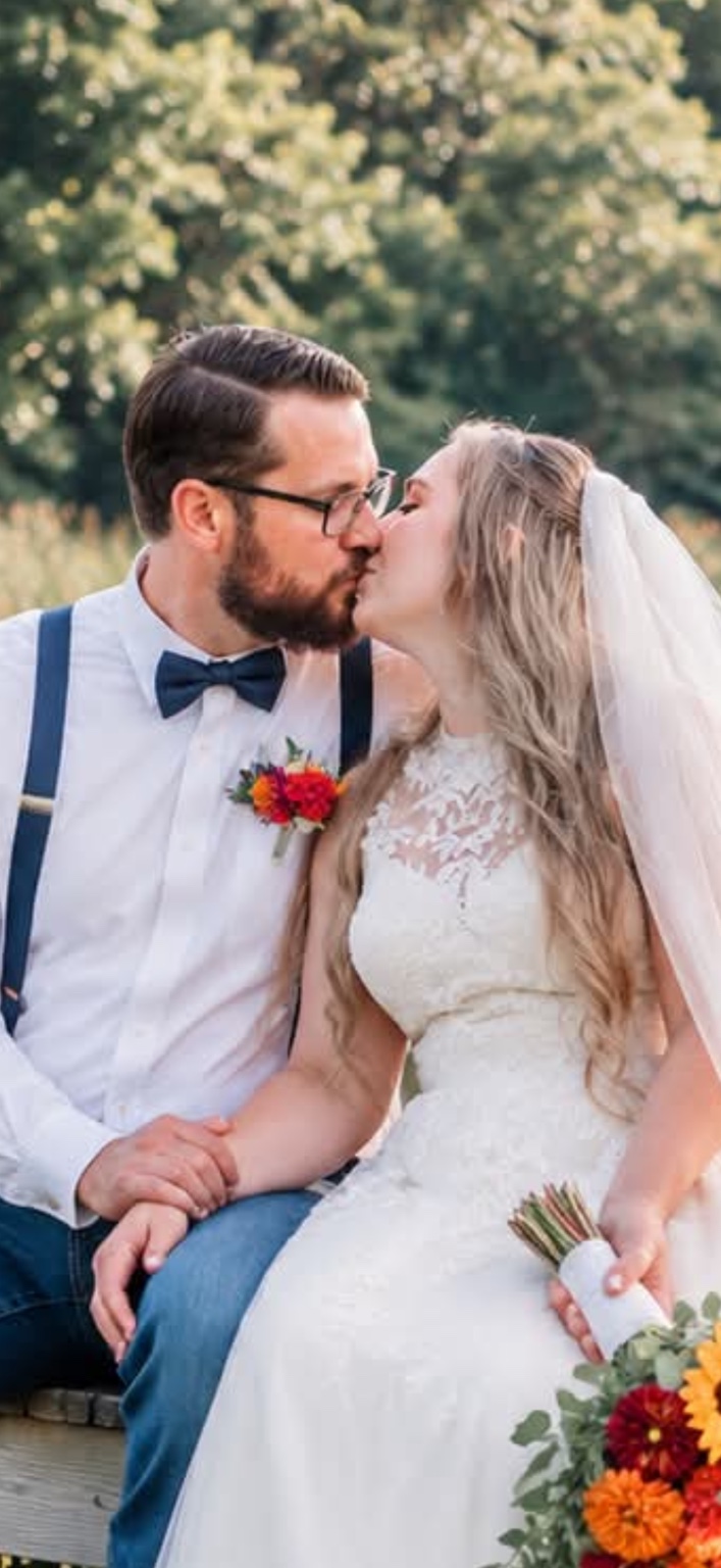 A seated bride and groom sharing a kiss outdoors